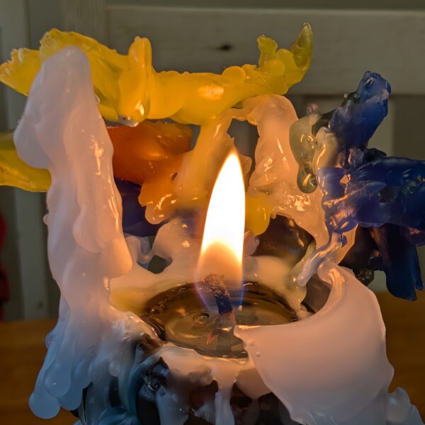 A candle burned nearly to the end, surrounded by different colored bits of wax.