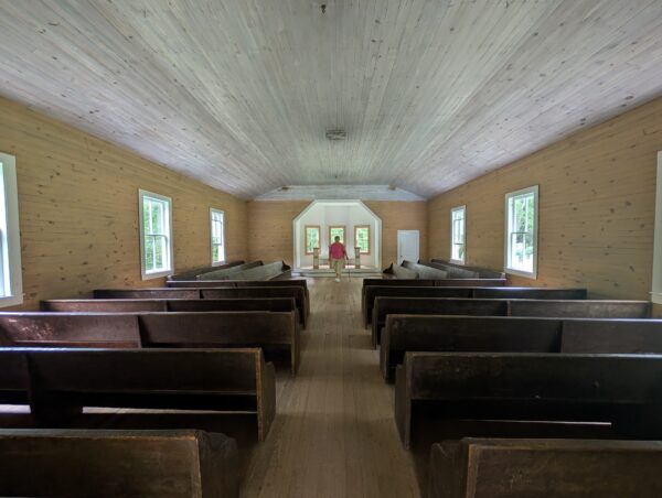 A long view down an unadorned wooden church house lined with pews.