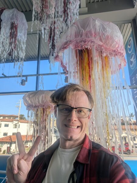 A selfie taken at the Monterey Bay National Marine Sanctuary Exploration Center in Santa Cruz, CA. Jellyfish sculptures hang from the ceiling behind Danny.