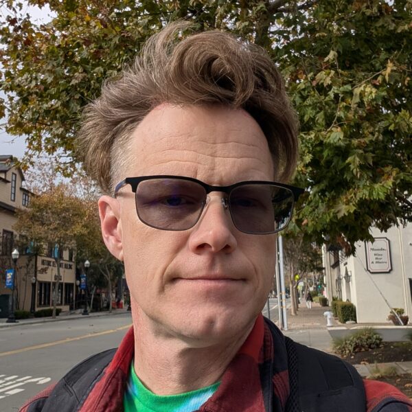 A headshot of Danny, for some reason. Big hair beneath a lush suburban tree canopy.