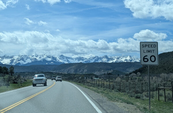 A two-lane highway, snow-capped mountains in the distance. To the right, a "Speed Limit 60" sign.
