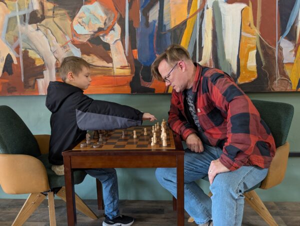 Younger son reaches over the board while Dad looks on.