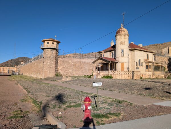An old masonry prison tower and wall, topped with three rows of fresh razor wire.