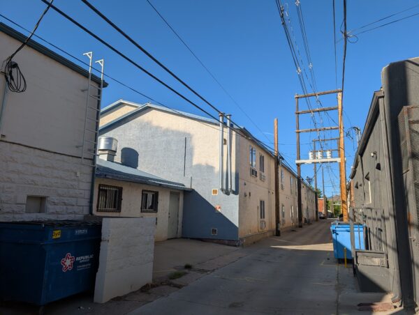 A view down an alleyway. The budget hotel is painted white, with an incomplete re-paint in blue.