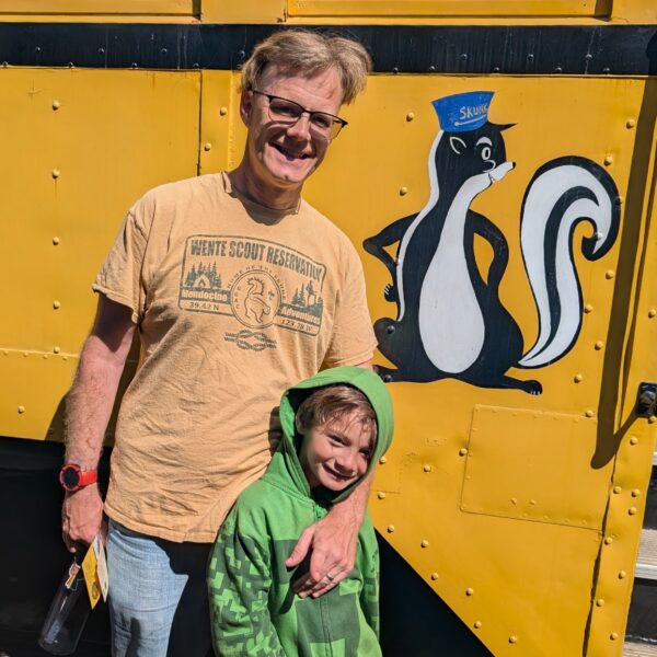 Danny and his younger son pose in front of the skunk character painted on the side of the yellow M200 railcar.